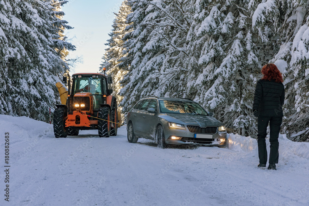 The tractor pulls a snowy car in the snow in winter landscape in Sumava. South Czech.