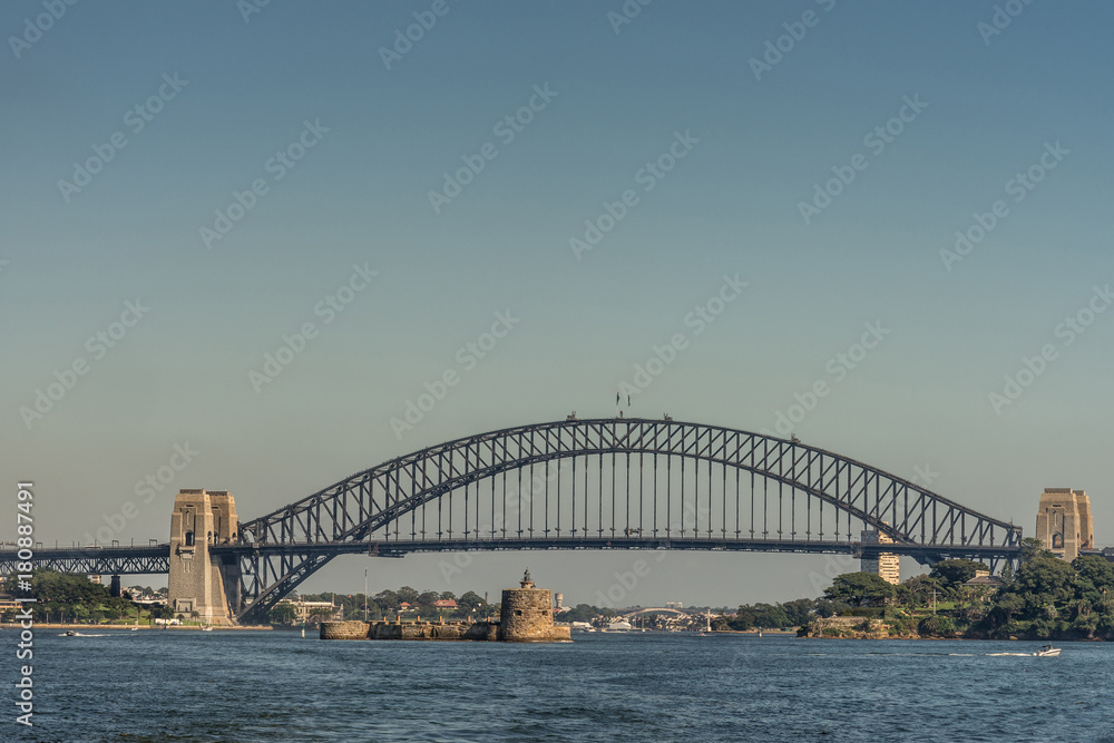 Sydney, Australia - March 26, 2017: Frontal view of black metalic Harbour Bridge including support towers on both sided seen off water under blue sky. Denison Fort in the bay and Kirribilli high 