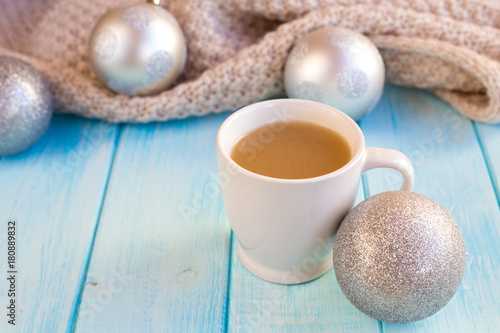 New Year's silver balls on a blue wooden background with a cup of hot tea or coffee and with a knitted scarf