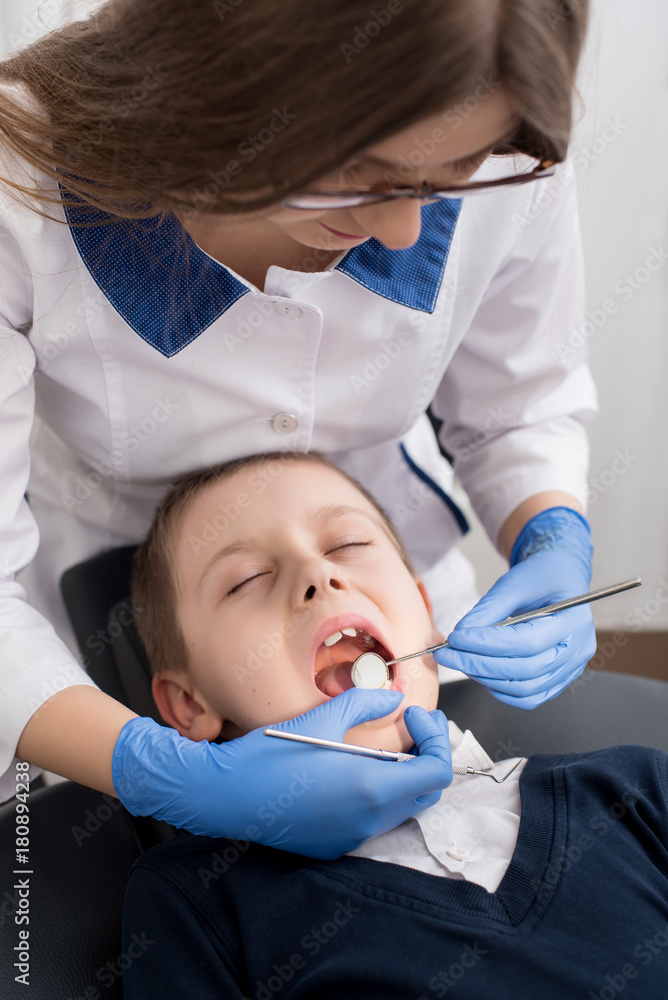 Female dentist examines the teeth of the patient child. Child mouth wide open in the dentist's chair. Close-up Female dentist examines the teeth of the patient child. Child mouth wide open in the dentist's chair. Close-up