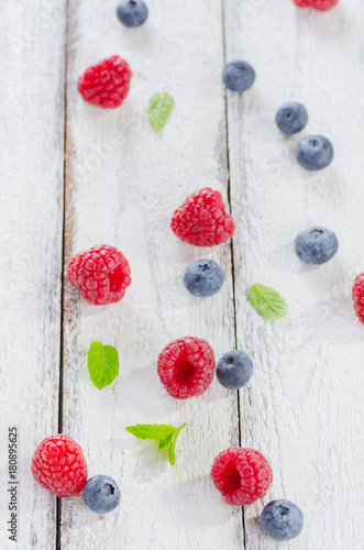 Raspberries and blueberries on white wooden background