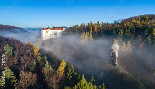 Fototapeta Wapienny klif Pieskowa Skala pod Krakowem, z izolowaną skałą „Maczuga Herkuklesa” (Hercules cudgel lub pałka) i zabytkowym renesansowym zamkiem w porannej mgle jesienią. Panorama z lotu ptaka