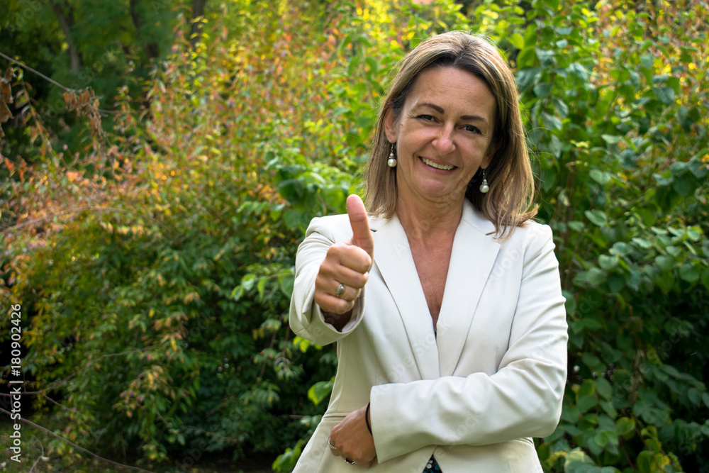Happy businesswoman showing thumbs up in nature and looking at camera. Happy businesswoman showing thumbs up in nature and looking at camera.