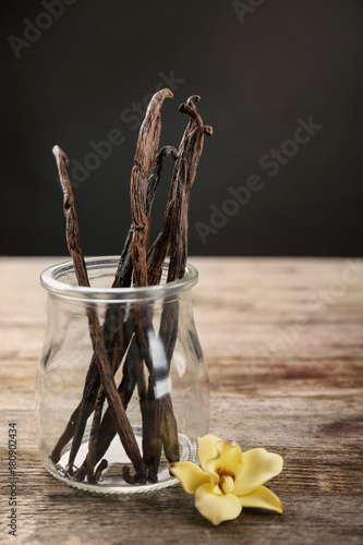 Dried vanilla pods in glass jar and flower on table