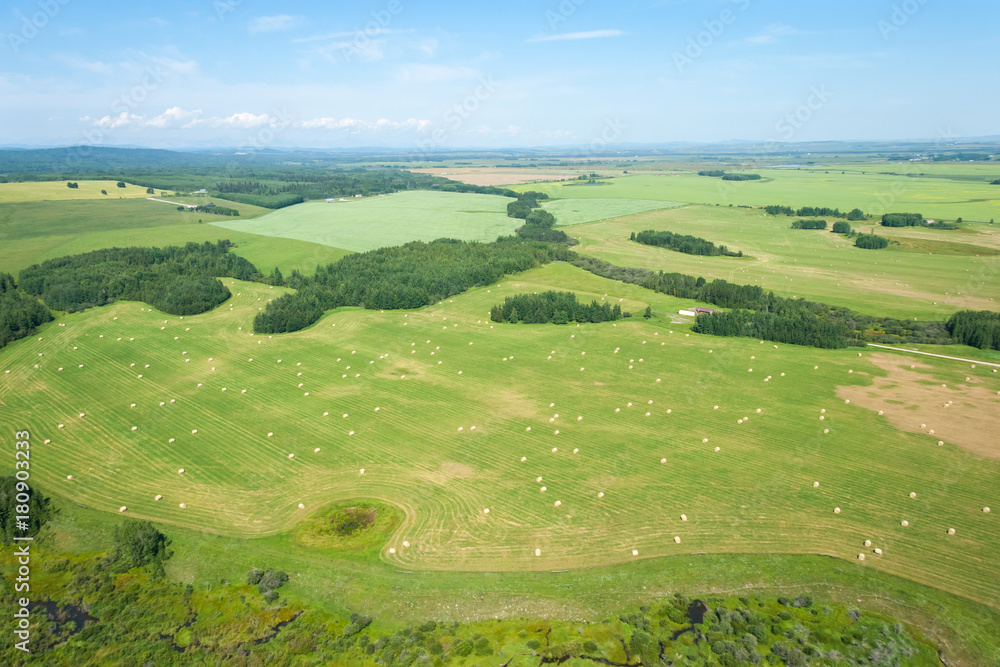 An aerial photo of green farm land with hey barrels and blue sky.