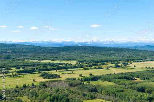 Aerial photo of forest and man made farmers fields with Rocky Mountains on the horizon.