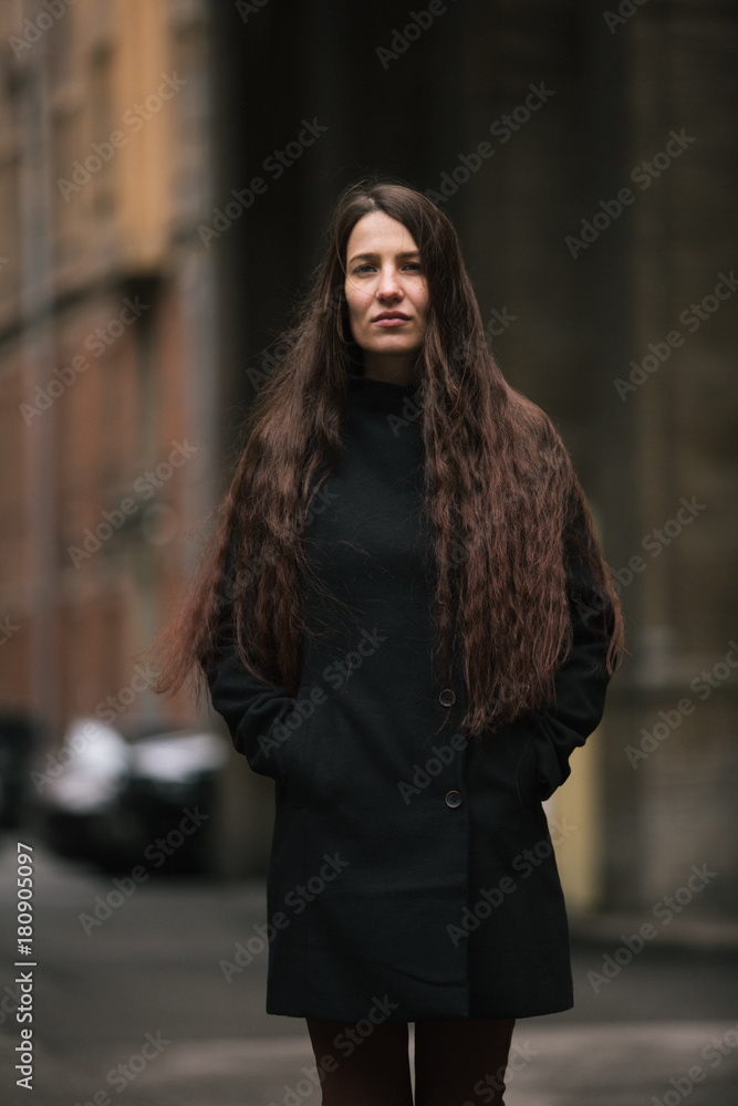 Style girl in black coat standing in a yard. Photo in black and white style.