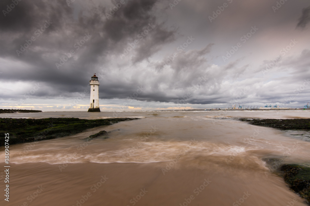 Water rushes over the beach in New Brighton, with the lighthouse contrasting against the dark sky.