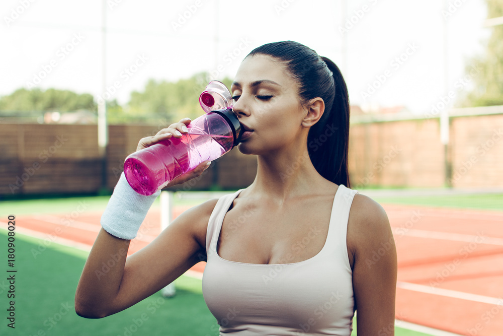 Beautiful teen girl holding bottle of water, smiling and drinking fresh  water Stock Photo