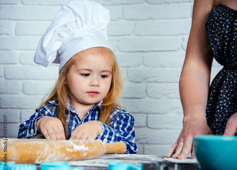 Child cook in chef hat helping mother Child cook in chef hat helping mother