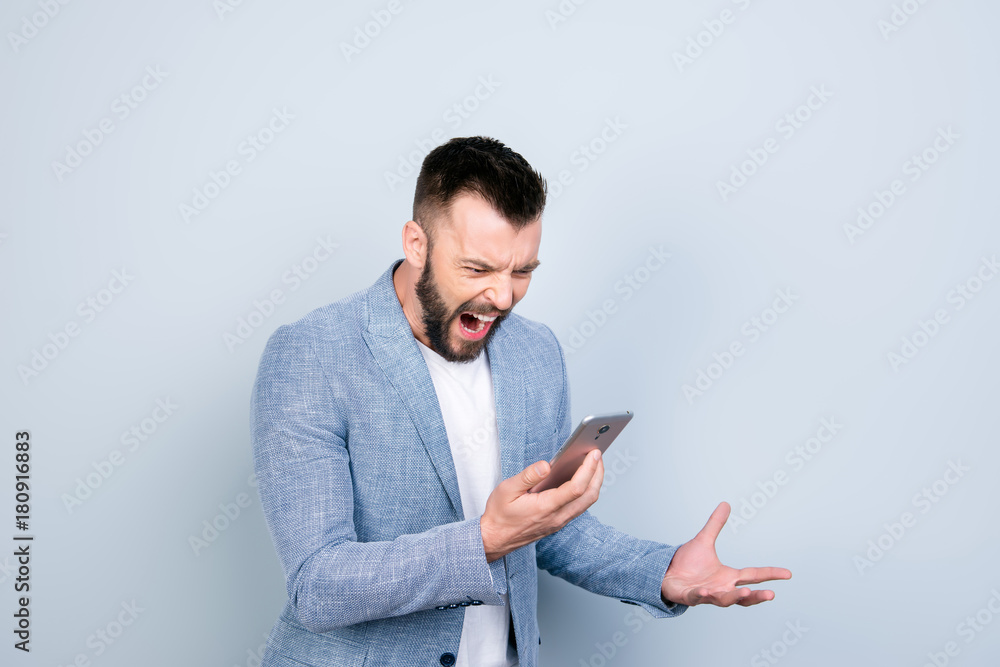Going crazy and insane, psycho and agression. Close up portrait of shouting stressed young brunet bearded entrepreneur, yell at his phone, on pure light background, wearing casual smart Going crazy and insane, psycho and agression. Close up portrait of shouting stressed young brunet bearded entrepreneur, yell at his phone, on pure light background, wearing casual smart
