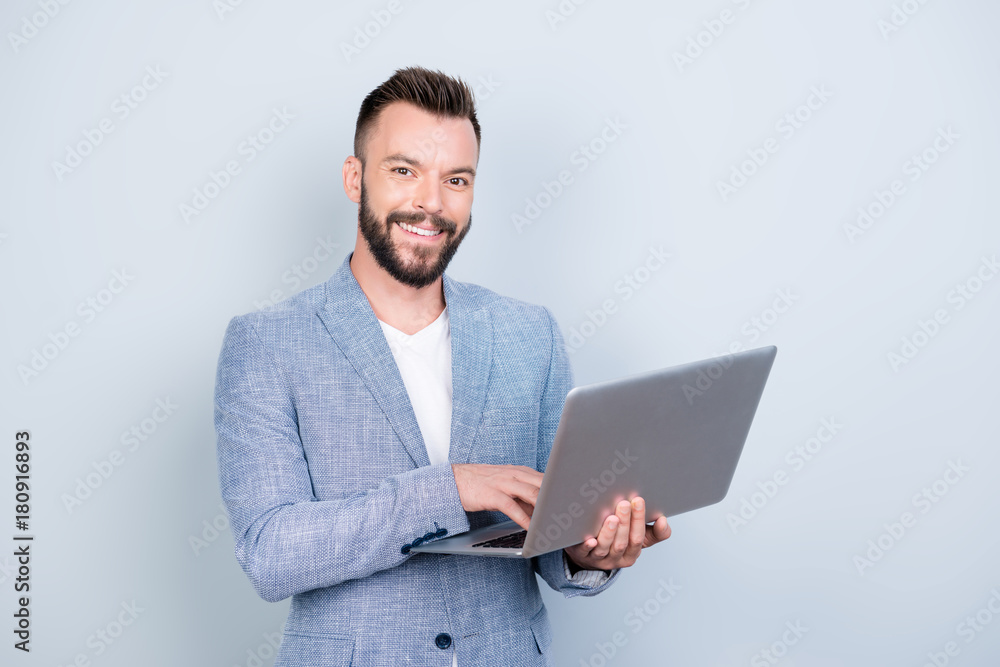 Close up portrait of cheerful brunet bearded business man in formal wear, typing on his laptop, he is a successful lawyer, standing browsing on his device, blue background Close up portrait of cheerful brunet bearded business man in formal wear, typing on his laptop, he is a successful lawyer, standing browsing on his device, blue background