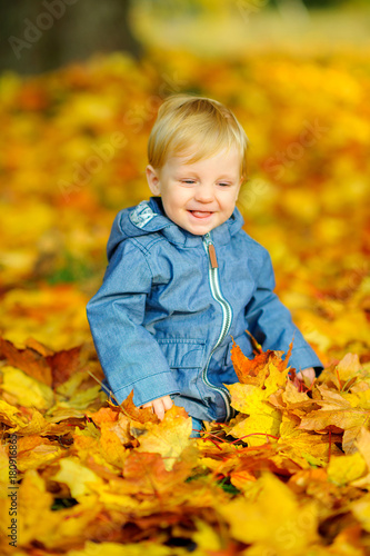 happy kid playing sitting in beautiful fallen leaves.