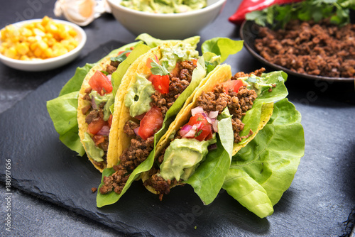 mexican taco corn shells stuffed with fried ground beef, tomato salsa and guacamole on a dark slate plate