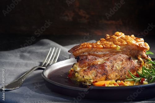 juicy roast pork with crunchy crust, rosemary and vegetables on a gray napkin against a rustic dark background, moody light, copy space