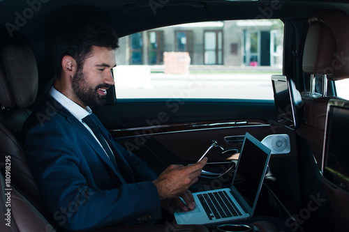 Great email. Side view of handsome young man using laptop and using his smart phone while sitting in car © MARIIA