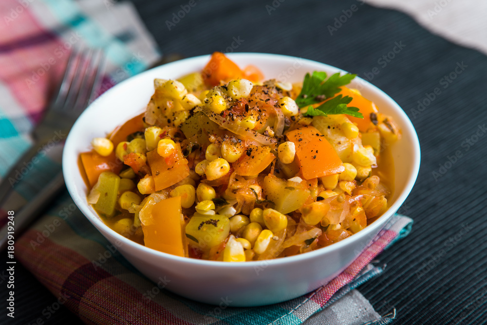 Vegetable stew with corn, sweet pepper, zucchini in a white plate on the table, top view Vegetable stew with corn, sweet pepper, zucchini in a white plate on the table, top view