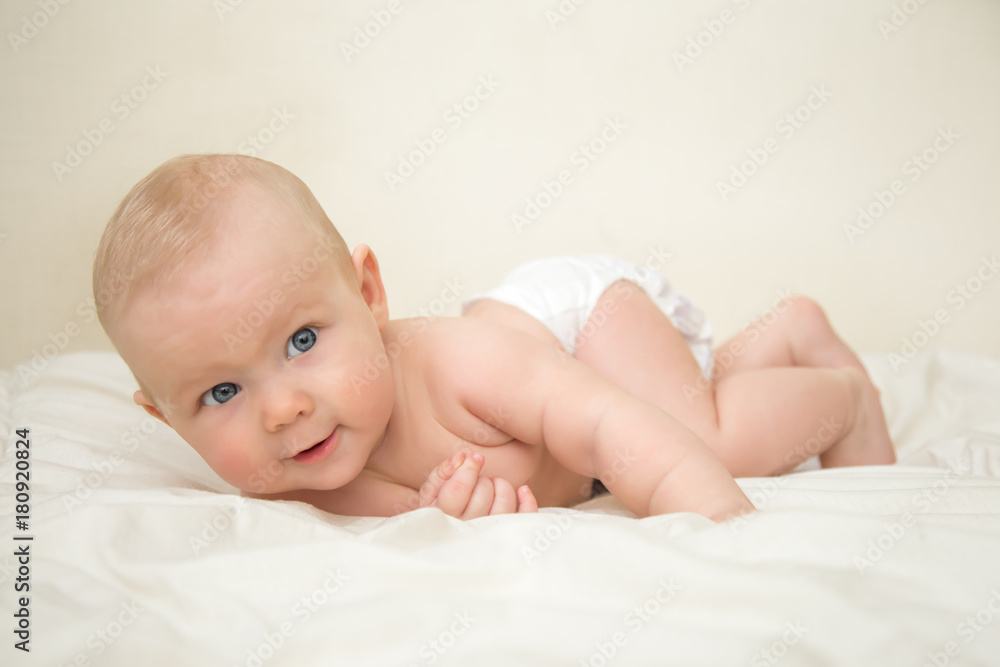Beautiful smiling cute blonde baby girl with blue eyes lying on the bed in the room. Happy child Beautiful smiling cute blonde baby girl with blue eyes lying on the bed in the room. Happy child