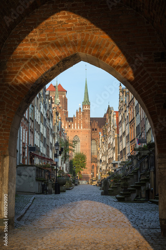 Old buildings on the St. Mary's Street (ul. Mariacka) and St. Mary's Church at the Main Town (Old Town) in Gdansk, Poland, viewed through an arched gateway in the morning.