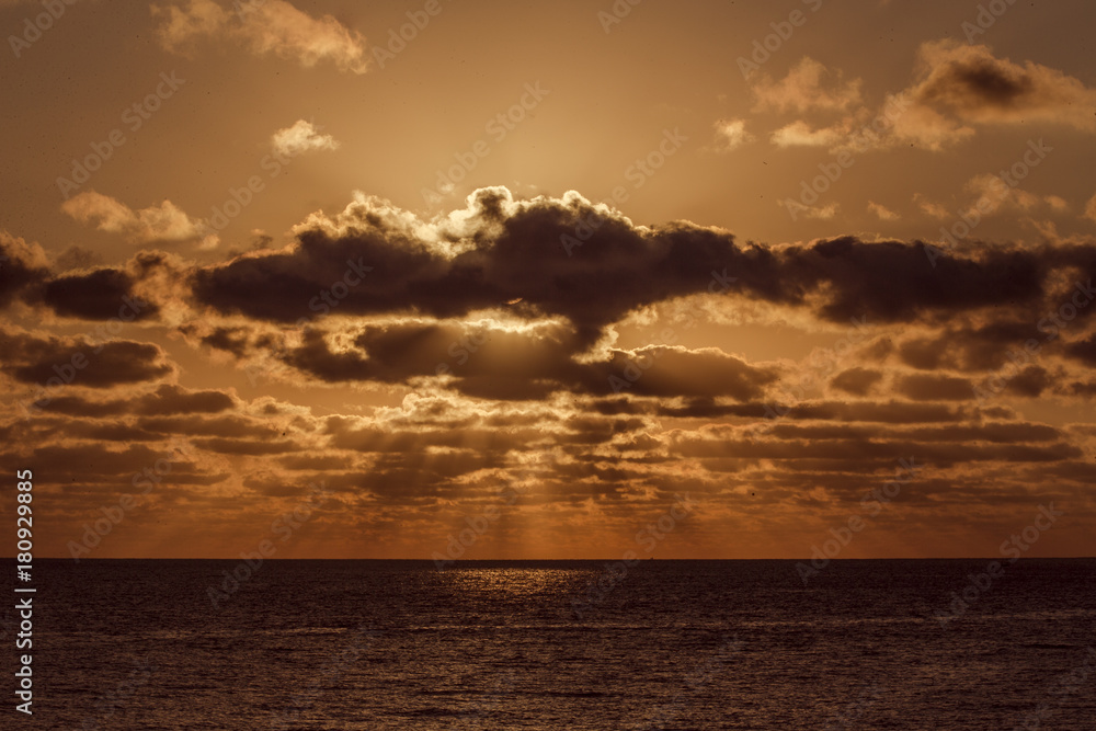 Romantischer Sonnenaufgang, Sonnenstrahlen leuchten orange durch Wolkenhimmel