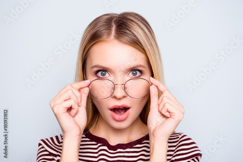 Wow! I don't believe you! Close up portrait of shocked astonished woman with open mouth and big eyes, she is touching her spectacles