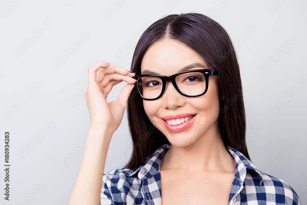 Close up portrait of charming smart lady with toothy smile, hazel eyes and beautiful face is touching her spectacles, dressed in casual checkered clothes isolated on grey background Close up portrait of charming smart lady with toothy smile, hazel eyes and beautiful face is touching her spectacles, dressed in casual checkered clothes isolated on grey background