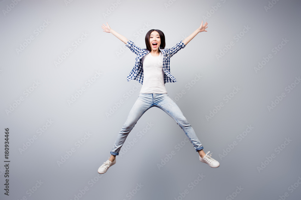 Concept of careless and madness. Crazy asian young girl is having fun. She is dressed in checkered shirt and jeans, she is isolated on grey background.