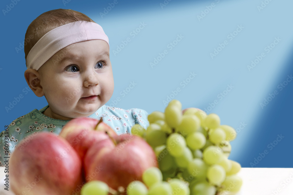 Positive toddler in front of a table with fresh fruit on a beautiful blue background