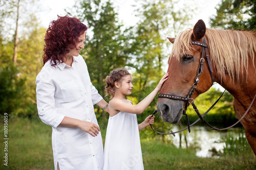 Mother and daughter are petting a horse. Summer meadow. © dinachi