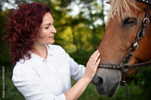 Beautiful woman is petting a horse. Summer meadow.