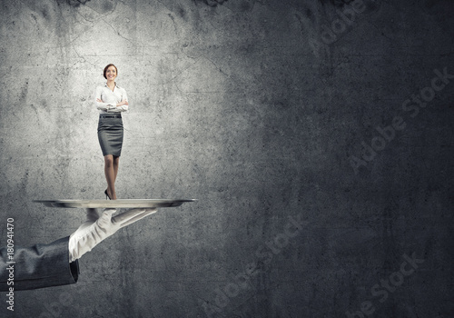 Confident elegant businesswoman presented on metal tray against concrete wall background