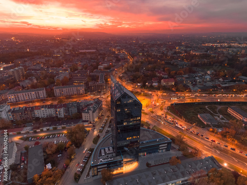 Modern architecture office building, Transportation, rush hour traffic, cars on highway interchange in city center. Sunset time, orange and gold light skyline. Drone aerial view of Krakow, Poland. 