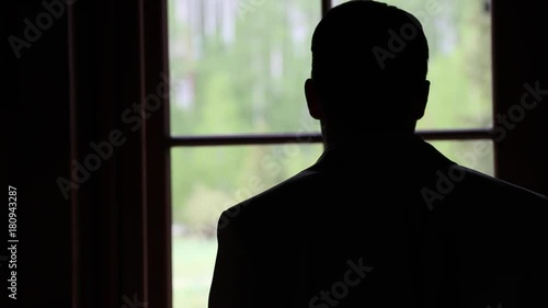 Silhouette man stands by window in contemplation, close up.