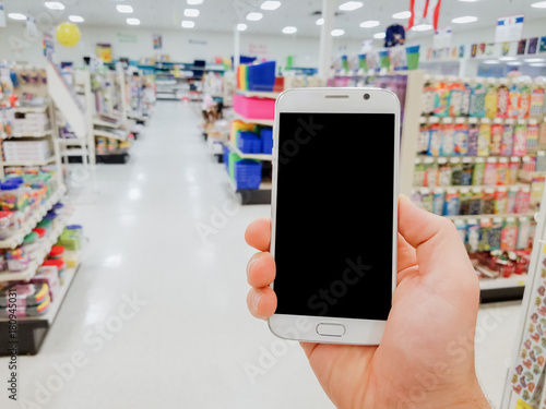 Hand holding mobile smart phone on Office supply shelf in store blur background