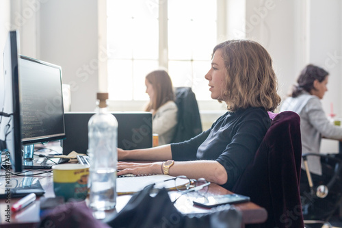 Women in startup business and entrepreneurship. Yound devoted female AI programmers and IT software developers team programming on desktop computer in startup company share office space. photo