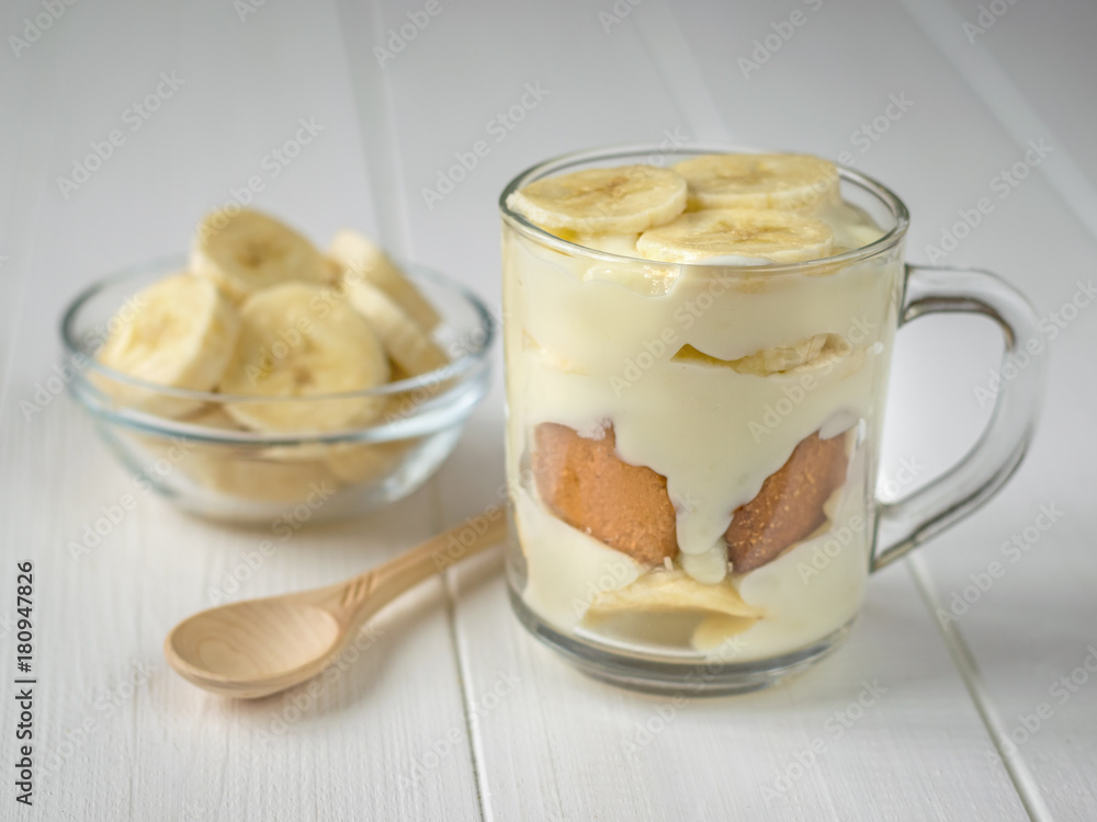 Banana pudding in a glass mug and a small spoon of light wood on the table. Banana pudding in a glass mug and a small spoon of light wood on the table.