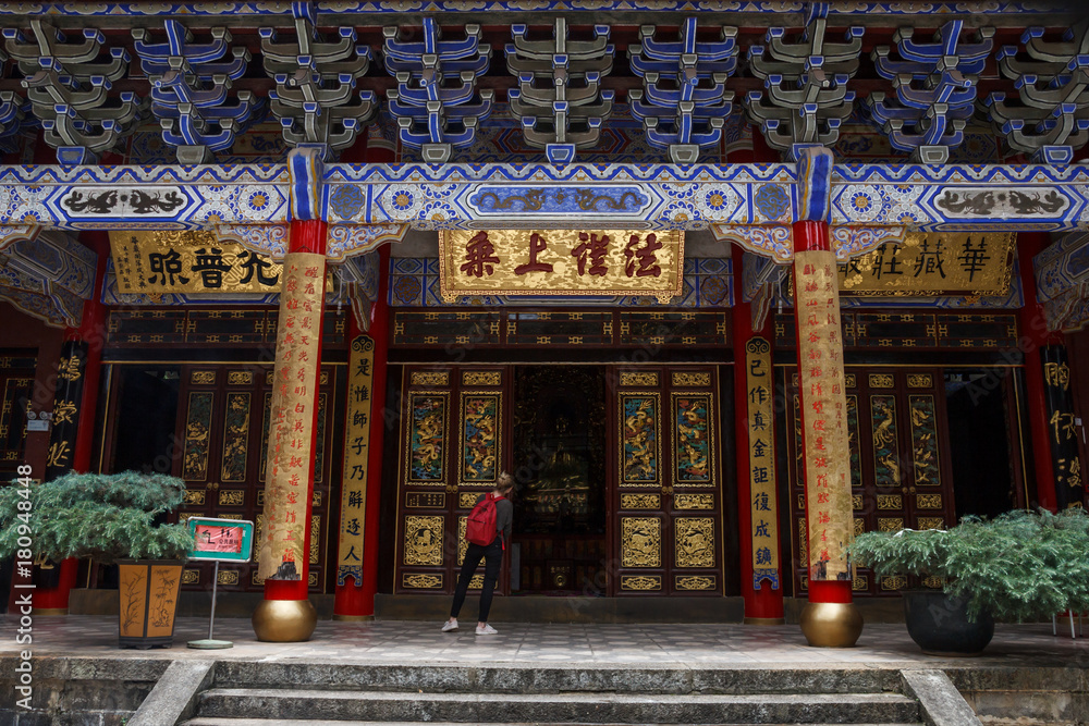 Tourist looking inside elegant red-golden gate in Chinese Buddhist temple Tourist looking inside elegant red-golden gate in Chinese Buddhist temple