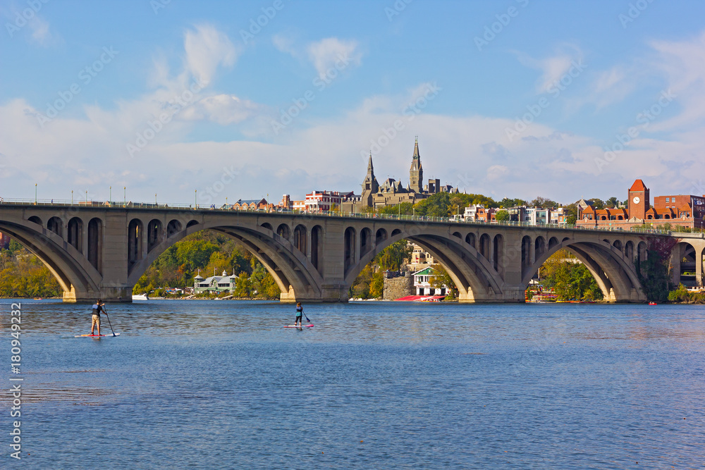 Fototapeta premium Young couple kayaking on Potomac River on a beautiful autumn afternoon near Key Bridge. Georgetown urban panorama near the water in Washington DC, USA.