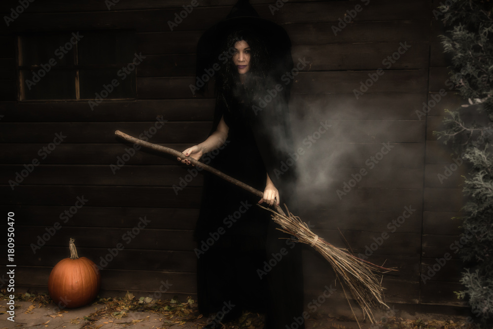Witch with broom and pumpkin standing in front of an old house, with ...