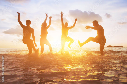 crowd of friends having fun in the water at sunset, silhouettes of happy people enjoying summer holidays