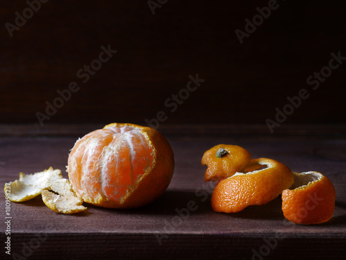 Half-peeled mandarin and peel on a wooden surface, minimalistic still life. Beautiful side light and dark background.