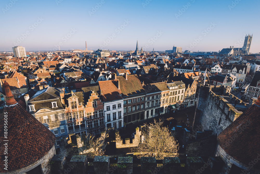 Fototapeta premium Ghent, Flanders, Belgium - December 30th, 2016. Gent Old town panoramic view from above Gravensteen castle. Ghent skyline with merchant houses roofs, St. Bavo and St.Jacob's cathedrals by golden hour.
