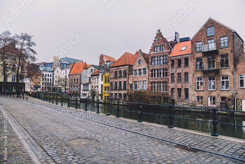 Ghent, Flanders, Belgium - January 1th, 2017. Medieval brick merchant houses near canal in Gent Old town. View from empty embankment by cloudy morning.