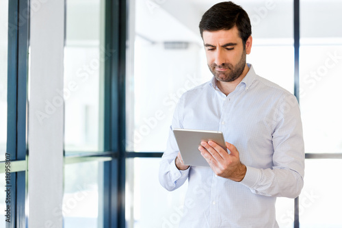 Young handsome businessman using his touchpad standing in office