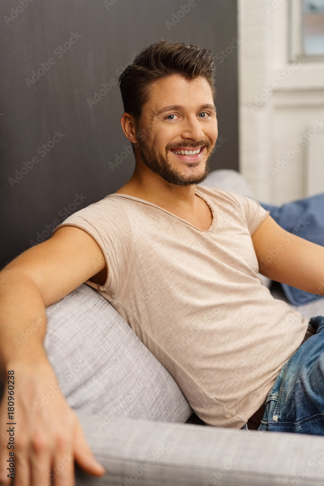lachender mann sitzt auf einem grauen sofa lachender mann sitzt auf einem grauen sofa