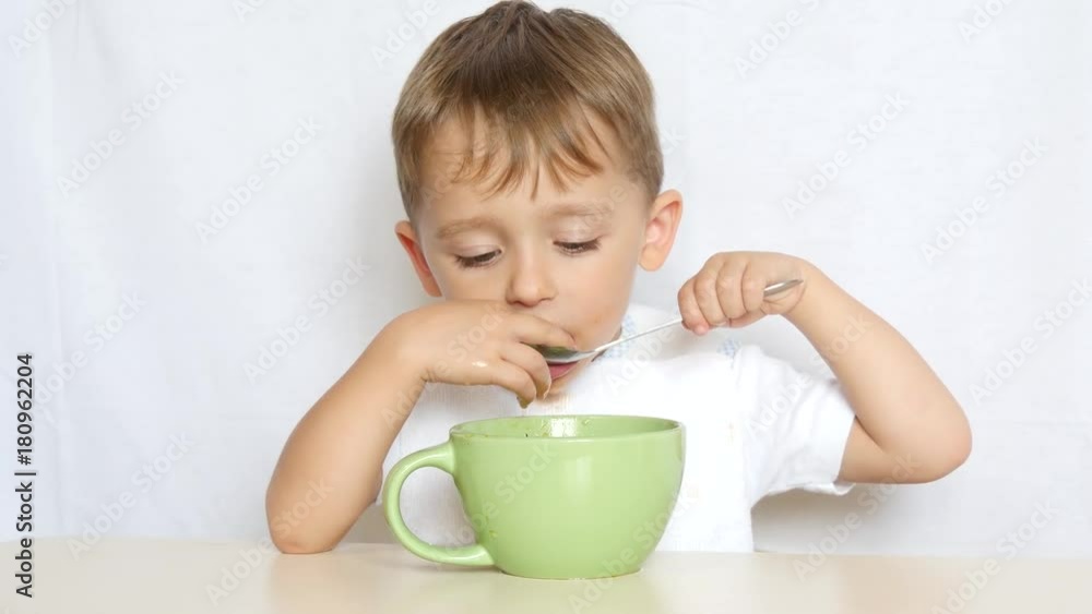 Child boy eating food with a spoon sitting at the table Child boy eating food with a spoon sitting at the table