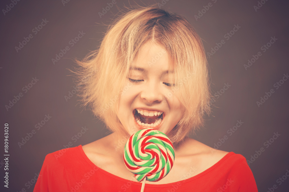 Blonde girl teenager in a red blouse bites a lollipop with a teeth.Toned