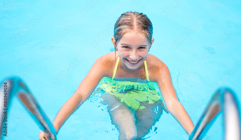 Cute smiling little girl in a swimming pool, looking into the camera ...