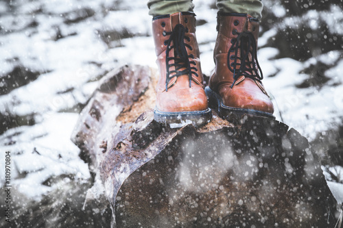 Girl standing on a tree stump in nature with falling snow.