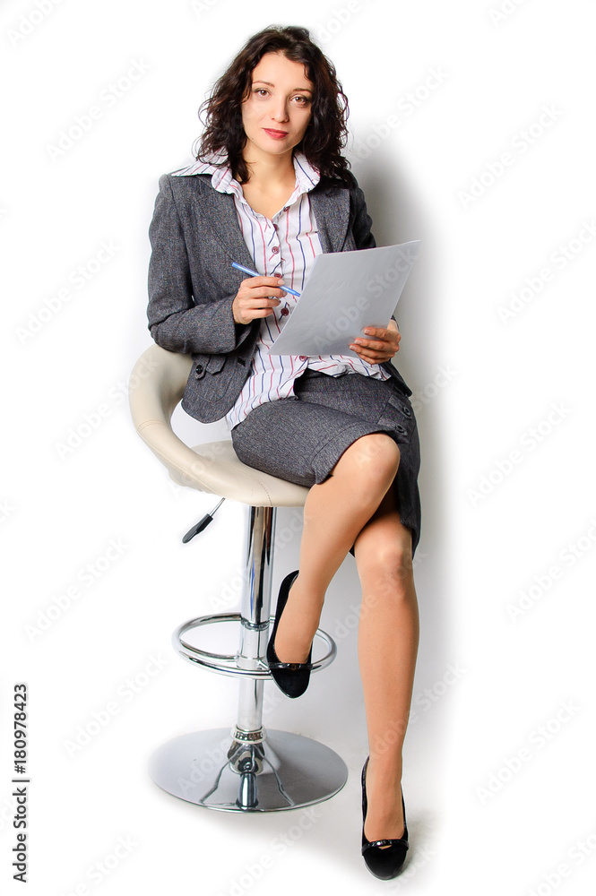 Business woman portrait. The brunette is walking on a high chair. He holds a sheet of paper and a ballpoint pen in his hands. Isolated Business woman portrait. The brunette is walking on a high chair. He holds a sheet of paper and a ballpoint pen in his hands. Isolated